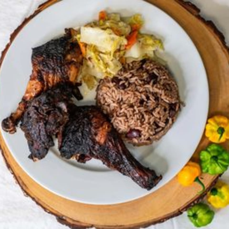 Caribbean jerk chicken with rice and peas, and steamed cabbage on a white plate.