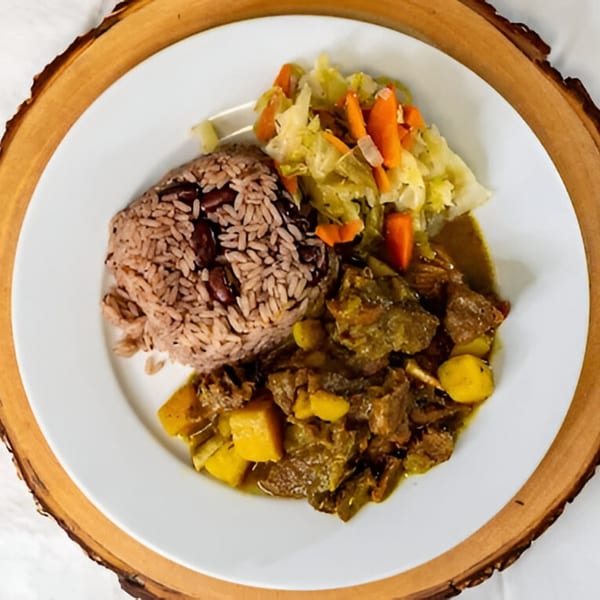 A Caribbean Spice! meal with rice and peas, curry goat, and steamed cabbage on a white plate.