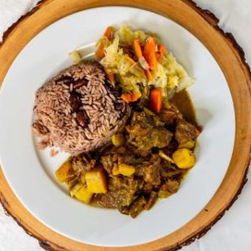 A Caribbean meal with rice and peas, curry goat, and steamed cabbage with carrots.