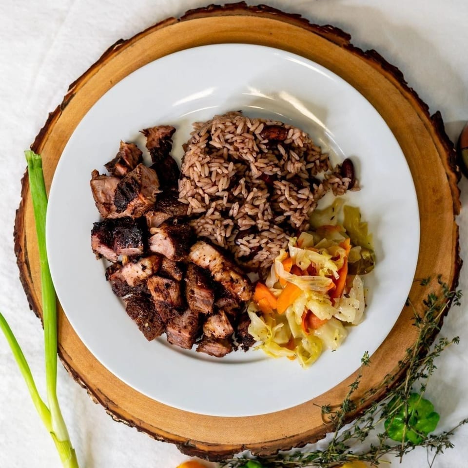 Caribbean jerk chicken with rice and peas, and steamed cabbage on a white plate.