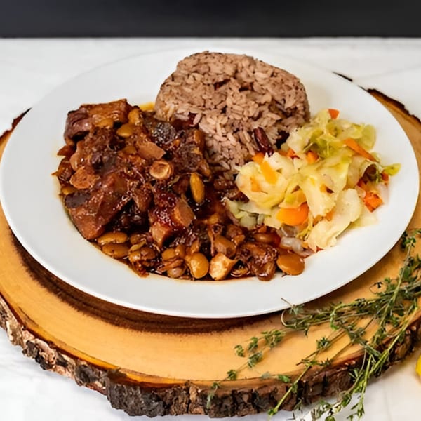 A Caribbean meal with brown stew chicken, rice and peas, and steamed cabbage on a white plate.