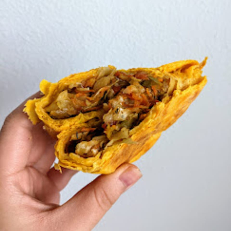 Hand holding a Caribbean Spice! vegetable patty, cut open to show the savory filling.