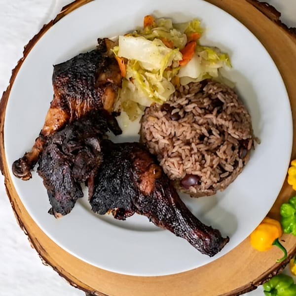 Two pieces of Caribbean jerk chicken with rice and peas, and steamed cabbage.