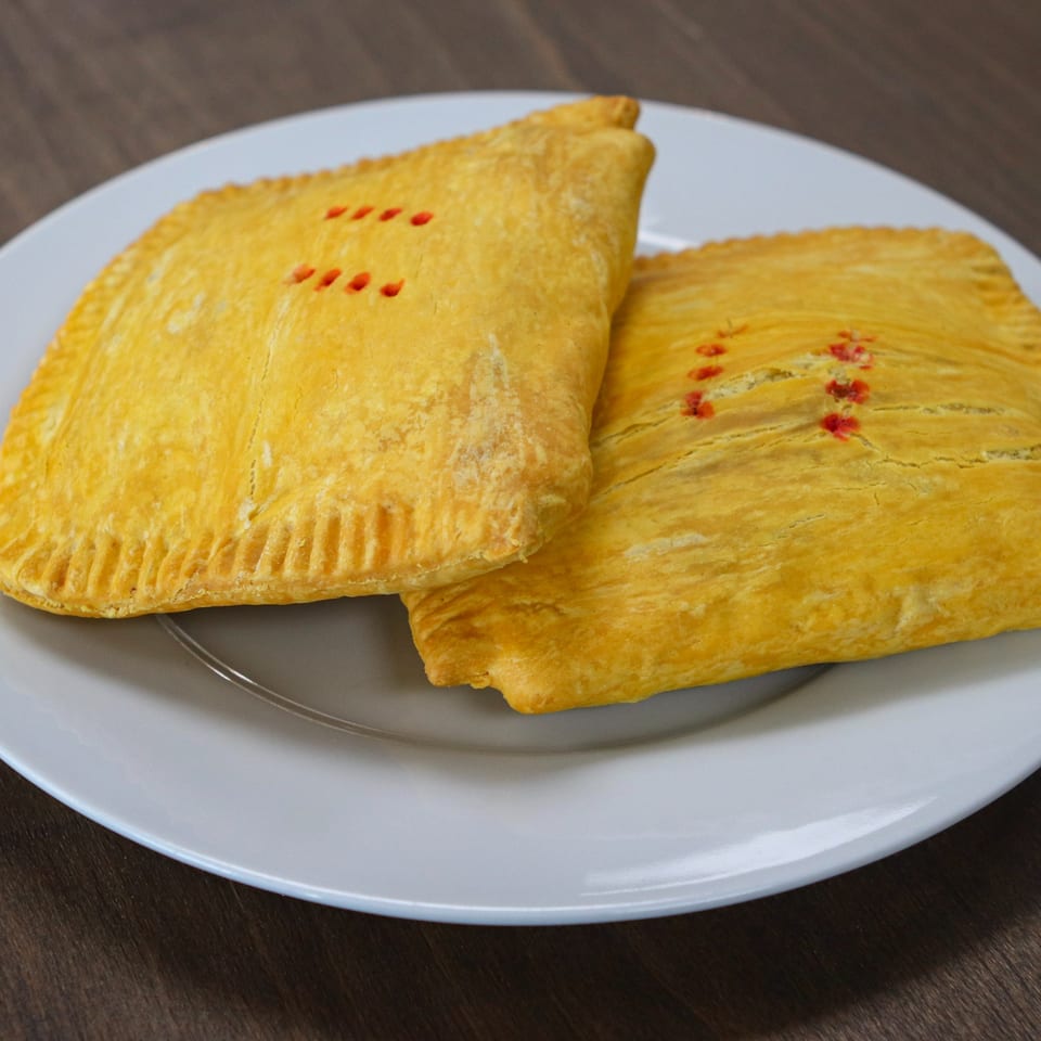 Two golden Caribbean beef patties with red markings, served on a white plate.